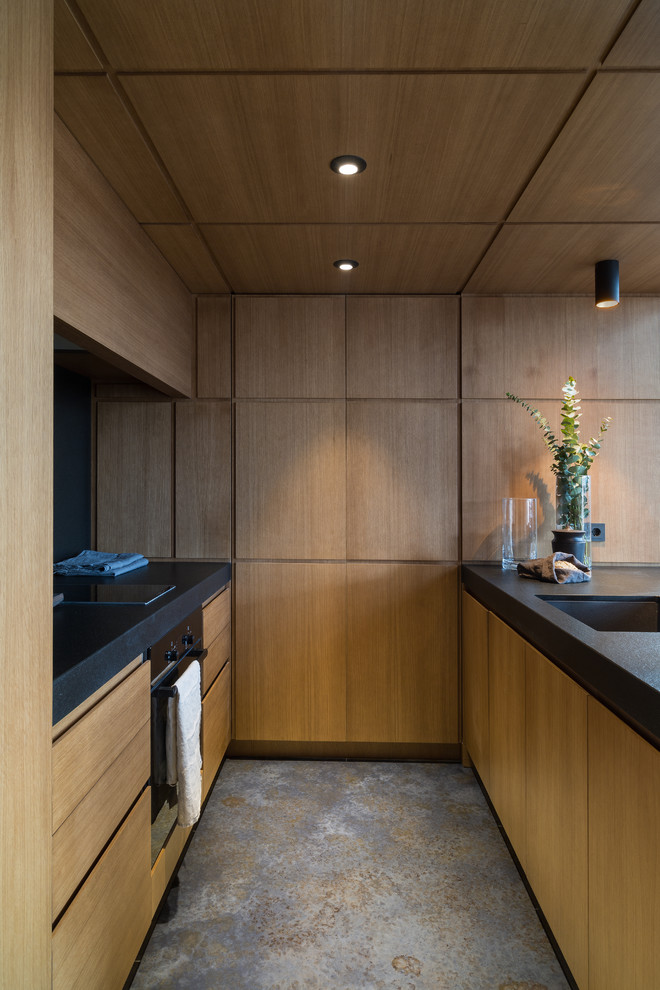 This is an example of a small contemporary galley open plan kitchen in Moscow with a submerged sink, flat-panel cabinets, medium wood cabinets, granite worktops, black splashback, an island and black worktops.