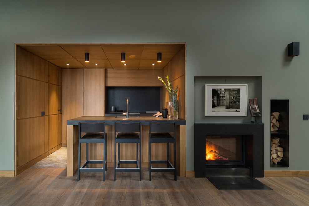 Cette image montre une petite cuisine ouverte parallèle design en bois brun avec un évier encastré, un placard à porte plane, un plan de travail en granite, une crédence noire, îlot et plan de travail noir.