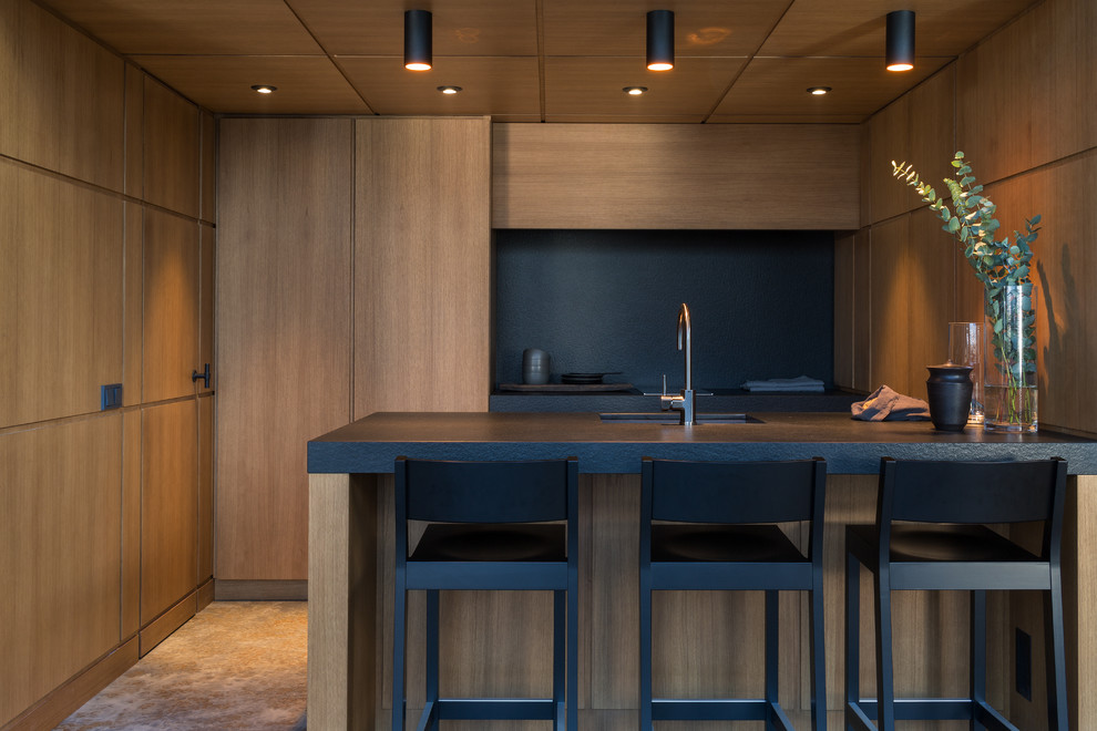 Idée de décoration pour une petite cuisine ouverte parallèle design en bois brun avec un évier encastré, un placard à porte plane, un plan de travail en granite, une crédence noire, îlot et plan de travail noir.