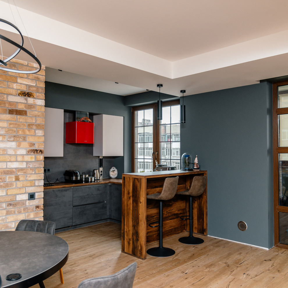На фото: п-образная кухня-гостиная у окна в стиле лофт с плоскими фасадами, серыми фасадами, серым фартуком и полуостровом с