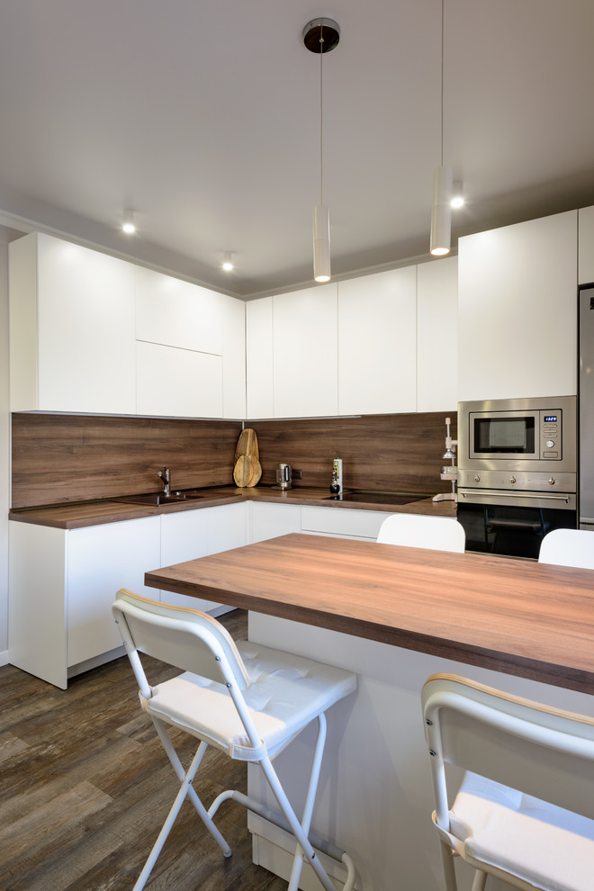 Modern inredning av ett stort brun brunt kök, med en nedsänkt diskho, släta luckor, vita skåp, träbänkskiva, brunt stänkskydd, stänkskydd i trä, rostfria vitvaror, vinylgolv, en köksö och brunt golv