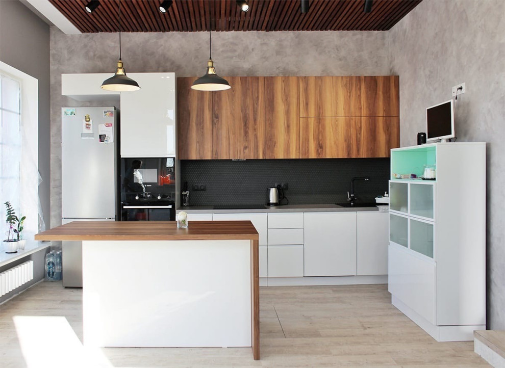 Idéer för att renovera ett stort funkis brun linjärt brunt kök och matrum, med en undermonterad diskho, släta luckor, vita skåp, träbänkskiva, svart stänkskydd, stänkskydd i mosaik, svarta vitvaror, vinylgolv, en köksö och beiget golv