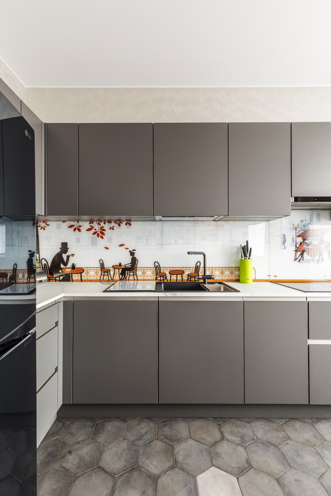 Modelo de cocinas en L actual con armarios con paneles lisos, puertas de armario grises, salpicadero multicolor, electrodomésticos negros, suelo gris y encimeras blancas