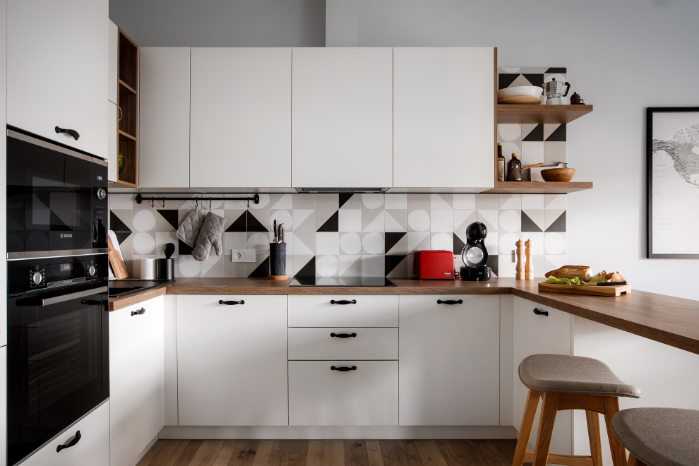 Design ideas for a scandi u-shaped kitchen in Yekaterinburg with flat-panel cabinets, white cabinets, wood worktops, multi-coloured splashback, black appliances, light hardwood flooring and a breakfast bar.