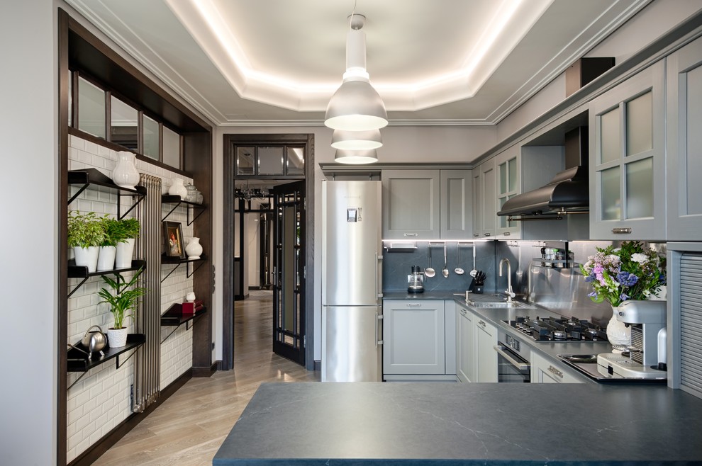 Inredning av ett klassiskt stort grå grått u-kök, med luckor med infälld panel, grå skåp, rostfria vitvaror, ljust trägolv, beiget golv, stänkskydd med metallisk yta och en halv köksö