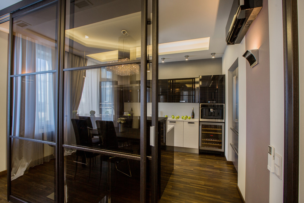 This is an example of a large contemporary galley enclosed kitchen in Moscow with flat-panel cabinets, white cabinets, white splashback, black appliances, brown floors and white worktops.