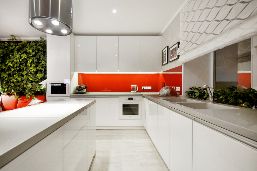 Foto de cocinas en L contemporánea abierta con fregadero integrado, armarios con paneles lisos, puertas de armario blancas, salpicadero rojo, electrodomésticos blancos, una isla y suelo de madera clara