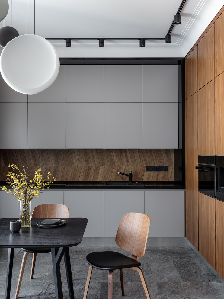 Idee per una cucina abitabile design con ante lisce, ante grigie, paraspruzzi marrone, elettrodomestici neri, pavimento grigio e top nero