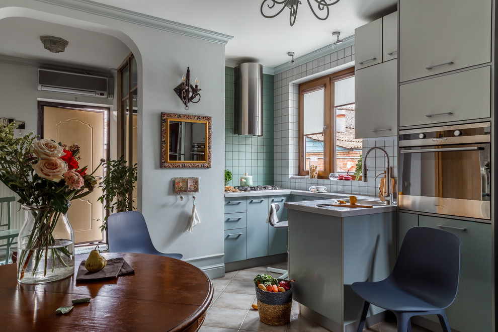 Inredning av ett modernt vit vitt kök, med släta luckor, blå skåp, grönt stänkskydd, stänkskydd i keramik, rostfria vitvaror, en halv köksö, beiget golv, en enkel diskho och bänkskiva i koppar