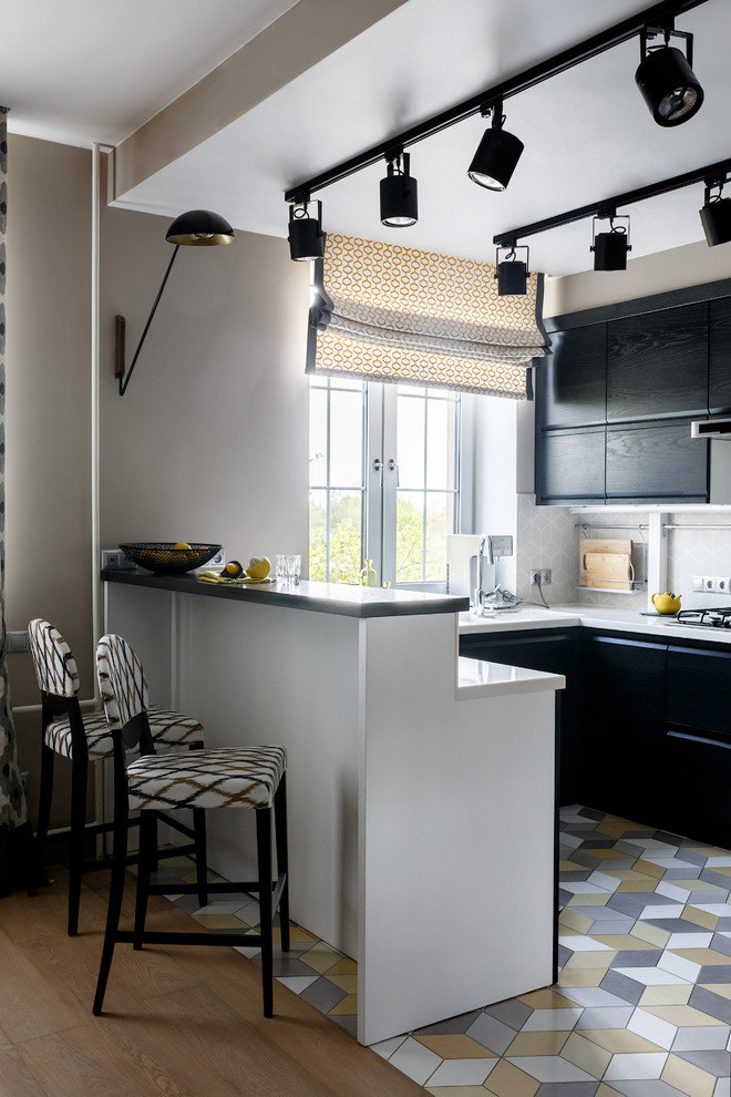 Идея дизайна: п-образная кухня-гостиная в современном стиле с плоскими фасадами, черными фасадами, полуостровом, серым фартуком, разноцветным полом, белой столешницей и барной стойкой