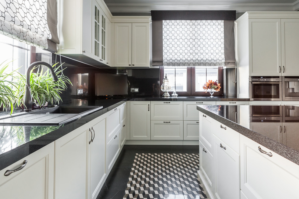 Klassisk inredning av ett avskilt u-kök, med en nedsänkt diskho, skåp i shakerstil, vita skåp, svart stänkskydd, rostfria vitvaror, en köksö och flerfärgat golv