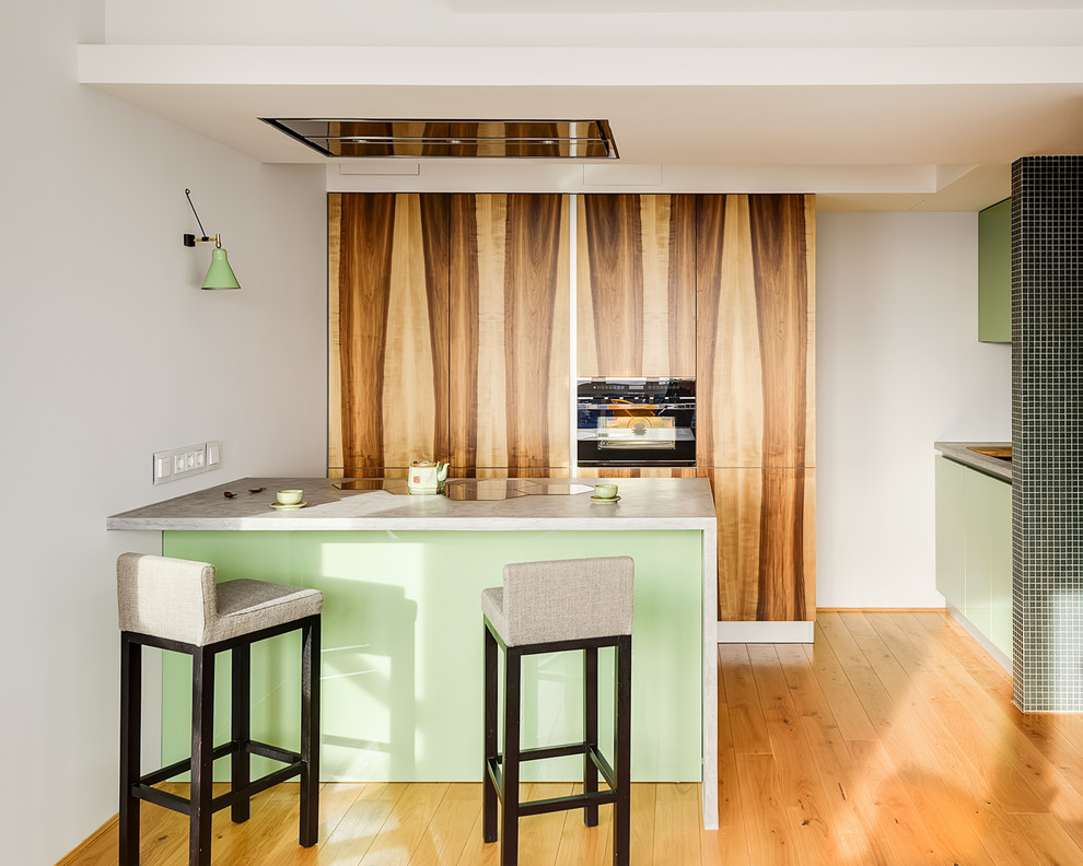 Foto på ett funkis grå kök, med en nedsänkt diskho, släta luckor, gröna skåp, bänkskiva i betong, svarta vitvaror, mellanmörkt trägolv, en köksö och brunt golv