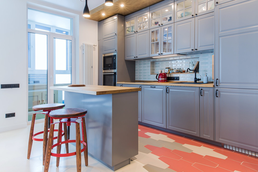Example of a trendy single-wall multicolored floor open concept kitchen design in Novosibirsk with a drop-in sink, raised-panel cabinets, gray cabinets, wood countertops, white backsplash, stainless steel appliances and an island