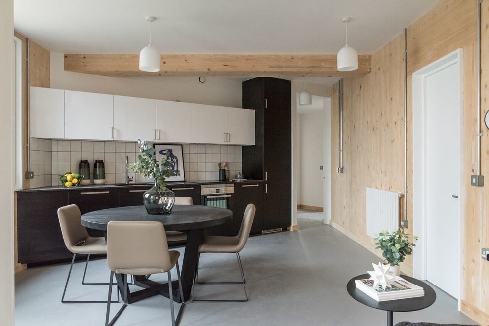 Свежая идея для дизайна: прямая кухня в скандинавском стиле с обеденным столом, одинарной мойкой, плоскими фасадами, белым фартуком, черной техникой, бетонным полом, серым полом и черно-белыми фасадами без острова - отличное фото интерьера