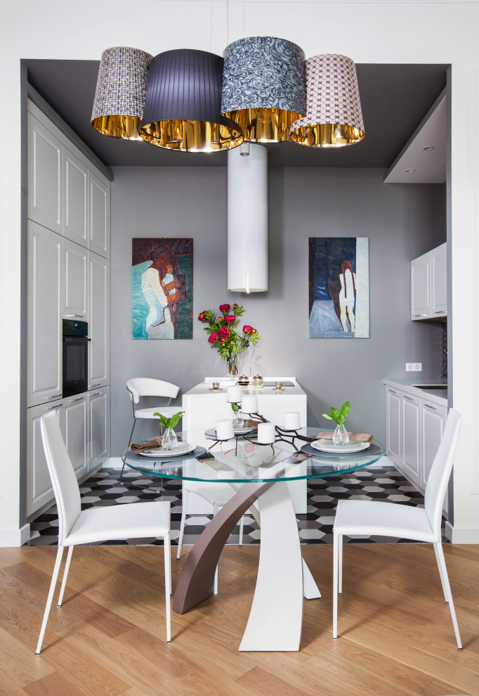 На фото: параллельная, светлая кухня в современном стиле с обеденным столом, фасадами с выступающей филенкой, белыми фасадами, черной техникой, полуостровом, разноцветным полом, белой столешницей и красивой плиткой с
