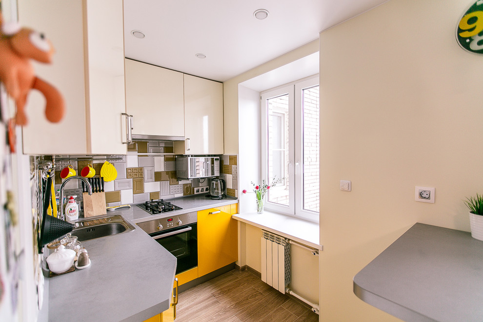 Foto på ett litet funkis kök, med en undermonterad diskho, släta luckor, gula skåp, laminatbänkskiva, flerfärgad stänkskydd, stänkskydd i keramik, rostfria vitvaror, laminatgolv och beiget golv