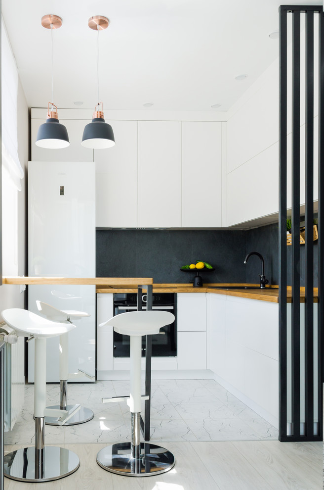 Design ideas for a small contemporary l-shaped open plan kitchen in Other with flat-panel cabinets, white cabinets, wood worktops, black splashback, porcelain splashback, white floors, a built-in sink, black appliances and brown worktops.
