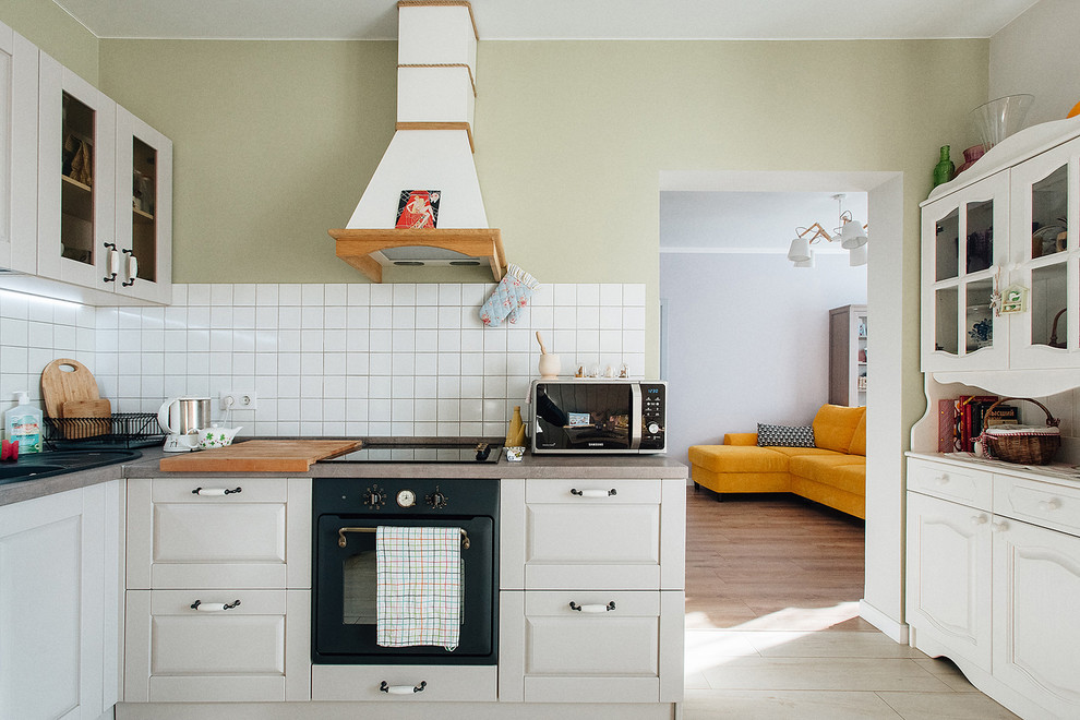 Modelo de cocina comedor nórdica con armarios con paneles con relieve, puertas de armario blancas, electrodomésticos negros y salpicadero blanco
