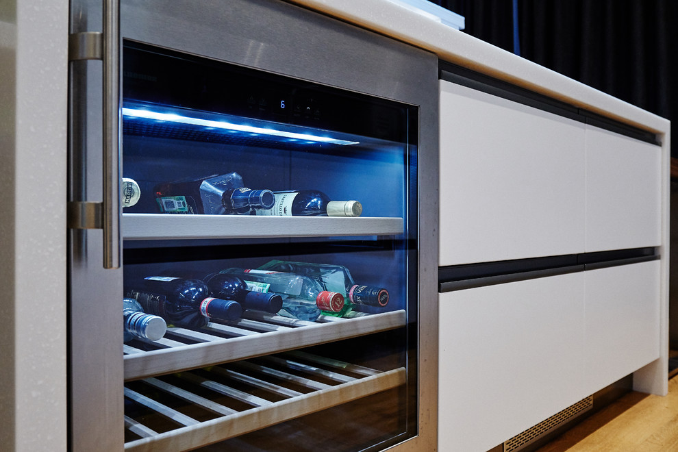 Modelo de cocina lineal actual de tamaño medio abierta con armarios con paneles lisos, puertas de armario blancas, salpicadero metalizado, una isla y encimeras blancas