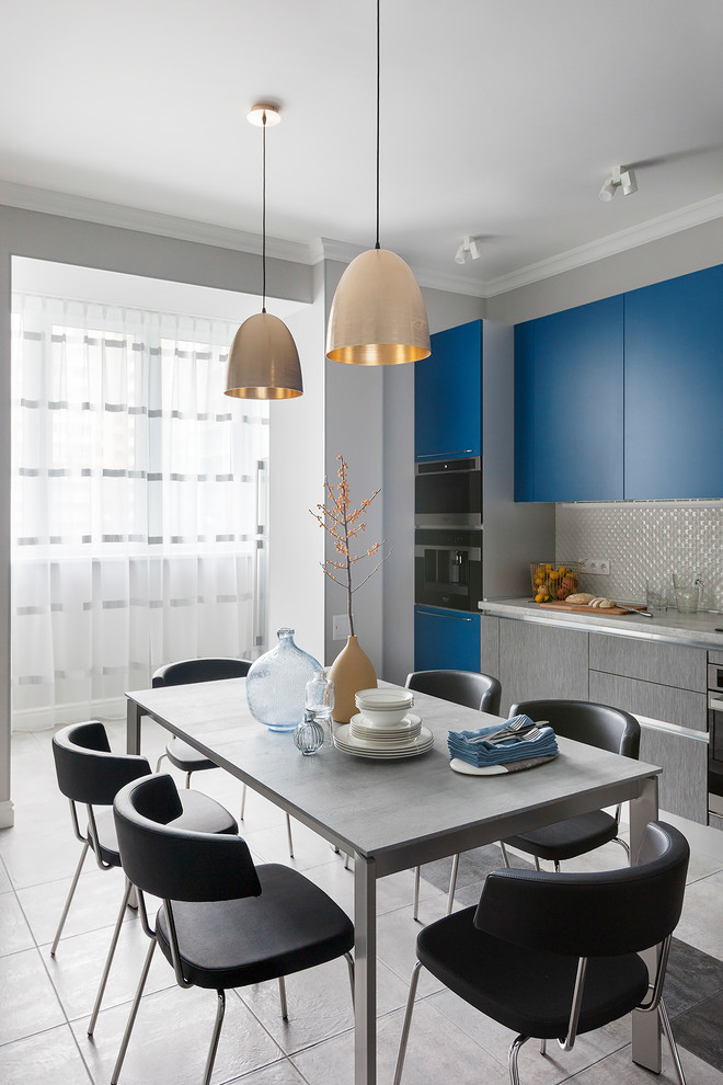 Modelo de cocina comedor contemporánea grande con armarios con paneles lisos, puertas de armario azules, salpicadero metalizado, electrodomésticos negros, suelo gris y encimeras grises
