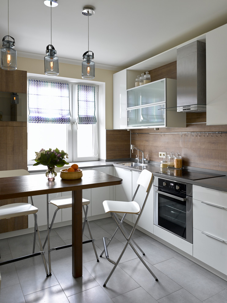 Foto de cocinas en L contemporánea cerrada con armarios con paneles lisos, puertas de armario blancas, salpicadero marrón, electrodomésticos de acero inoxidable y suelo gris