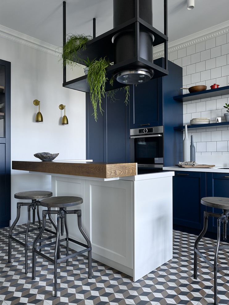 Foto på ett funkis vit linjärt kök, med en undermonterad diskho, skåp i shakerstil, blå skåp, vitt stänkskydd, rostfria vitvaror, en köksö och flerfärgat golv