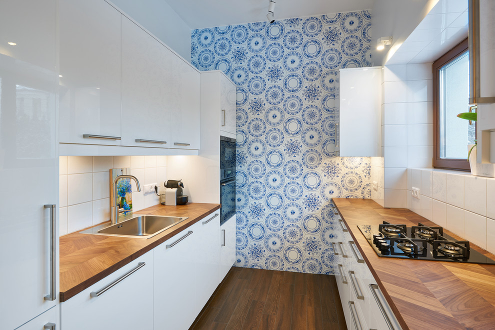 Inspiration for a medium sized contemporary galley enclosed kitchen in Moscow with flat-panel cabinets, white cabinets, a built-in sink, wood worktops, white splashback, integrated appliances and brown floors.