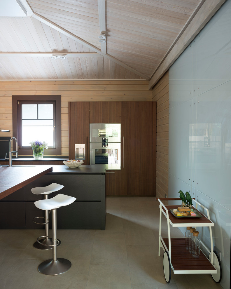 Cette image montre une grande cuisine design en U et bois brun fermée avec un évier intégré, une crédence noire, un électroménager en acier inoxydable, un sol en carrelage de porcelaine, îlot et un sol gris.