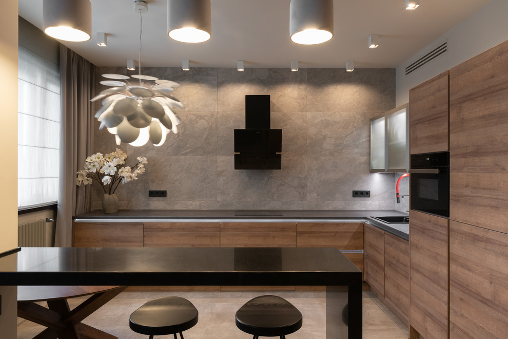 Inspiration for a contemporary l-shaped gray floor kitchen remodel in Moscow with a drop-in sink, flat-panel cabinets, medium tone wood cabinets, gray backsplash, black appliances, a peninsula and black countertops