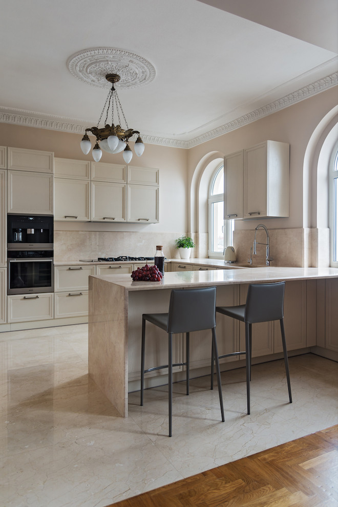 Eat-in kitchen - mid-sized transitional u-shaped marble floor and beige floor eat-in kitchen idea in Other with a drop-in sink, recessed-panel cabinets, beige cabinets, marble countertops, beige backsplash, marble backsplash, black appliances, an island and beige countertops