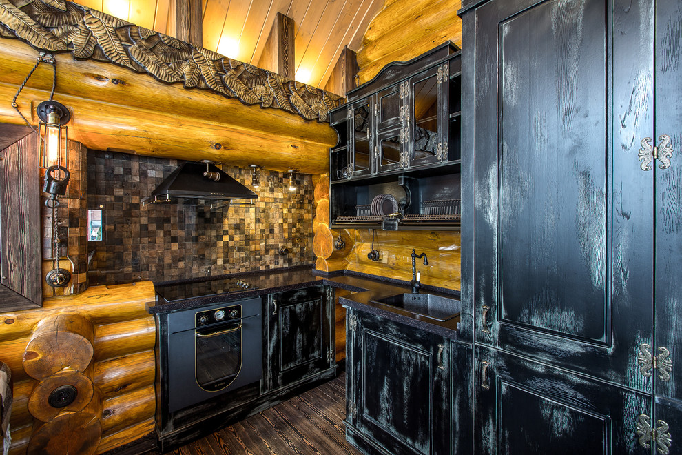 Diseño de cocina rural sin isla con fregadero encastrado, puertas de armario con efecto envejecido, electrodomésticos negros y suelo de madera oscura