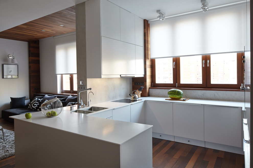 Immagine di una cucina contemporanea con lavello a doppia vasca, ante lisce, ante bianche, paraspruzzi bianco, parquet scuro, penisola e pavimento marrone