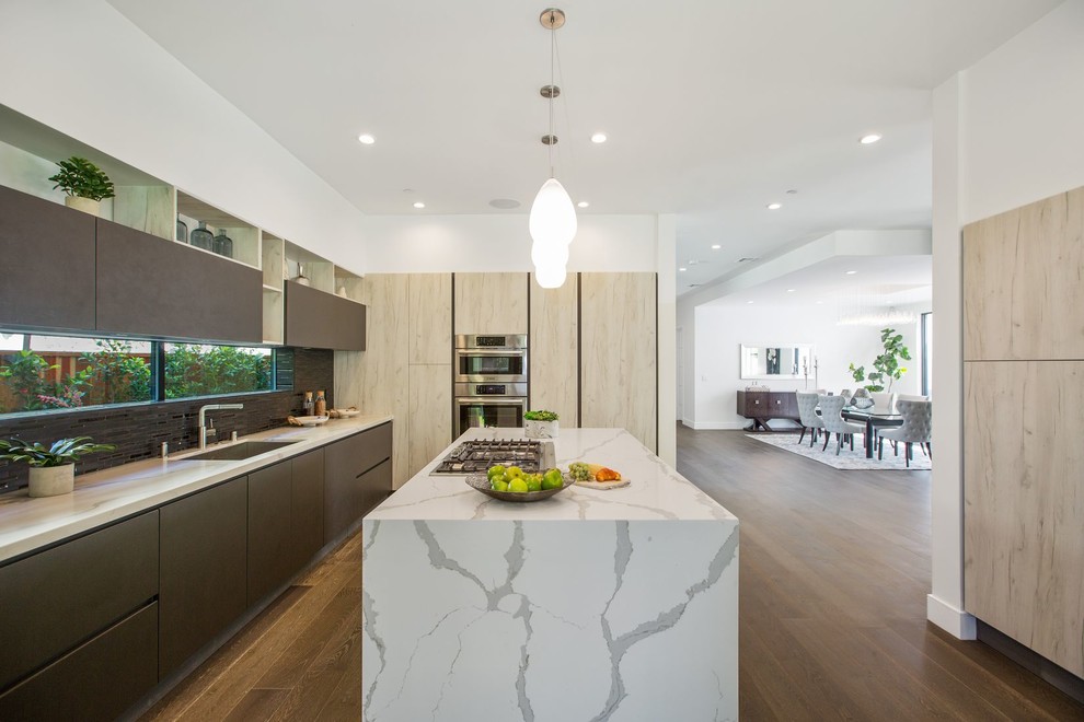 Moderne Küche in L-Form mit Unterbauwaschbecken, flächenbündigen Schrankfronten, hellen Holzschränken, Rückwand-Fenster, dunklem Holzboden, Kücheninsel und braunem Boden in Los Angeles