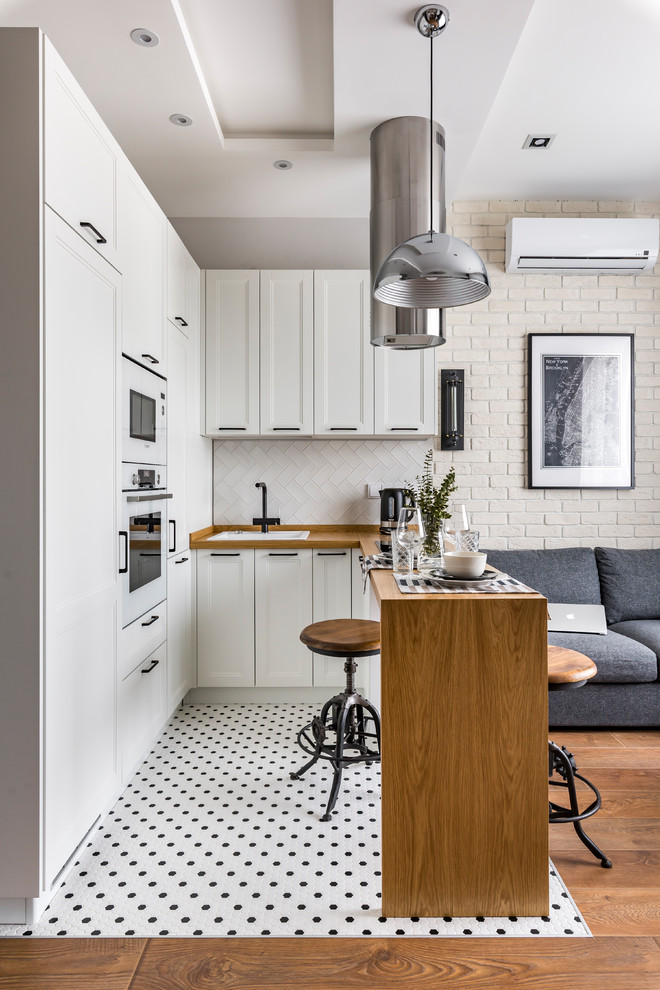 Inredning av ett modernt litet brun brunt kök, med en nedsänkt diskho, luckor med infälld panel, vita skåp, träbänkskiva, vitt stänkskydd, vita vitvaror, en halv köksö och flerfärgat golv