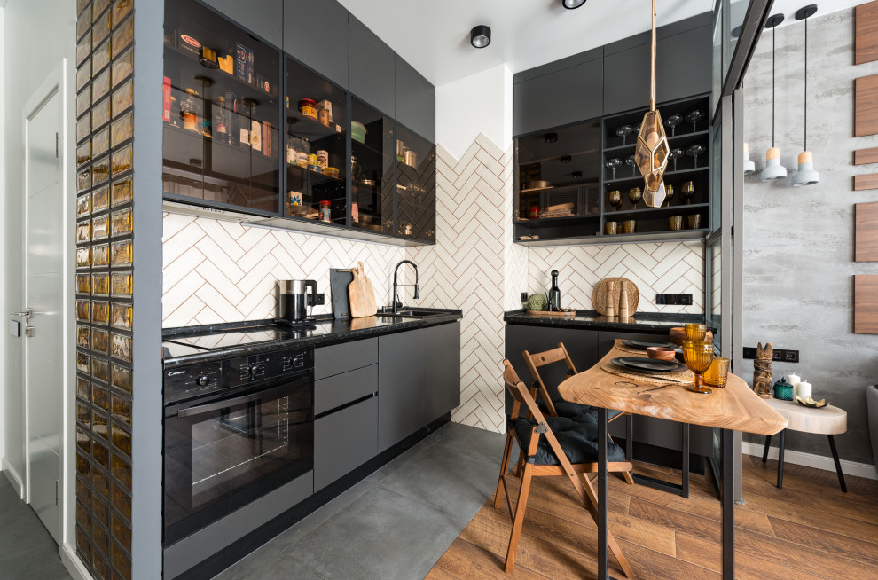 Foto de cocinas en L contemporánea abierta con armarios con paneles lisos, puertas de armario grises, salpicadero blanco, electrodomésticos negros, suelo gris y encimeras negras