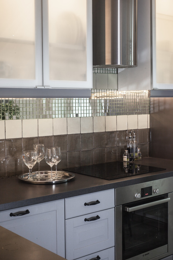 Bild på ett mellanstort funkis l-kök, med luckor med upphöjd panel, grå skåp, laminatbänkskiva, flerfärgad stänkskydd, spegel som stänkskydd och rostfria vitvaror