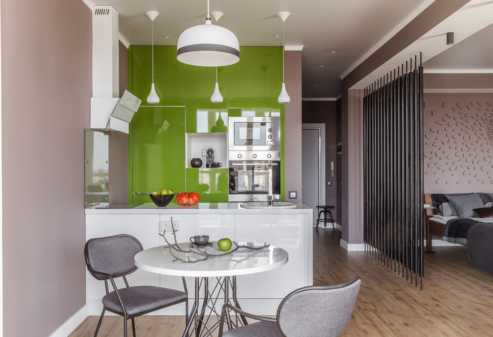Exempel på ett modernt vit linjärt vitt kök med öppen planlösning, med en nedsänkt diskho, släta luckor, gröna skåp, glaspanel som stänkskydd, rostfria vitvaror, cementgolv, en halv köksö och brunt golv