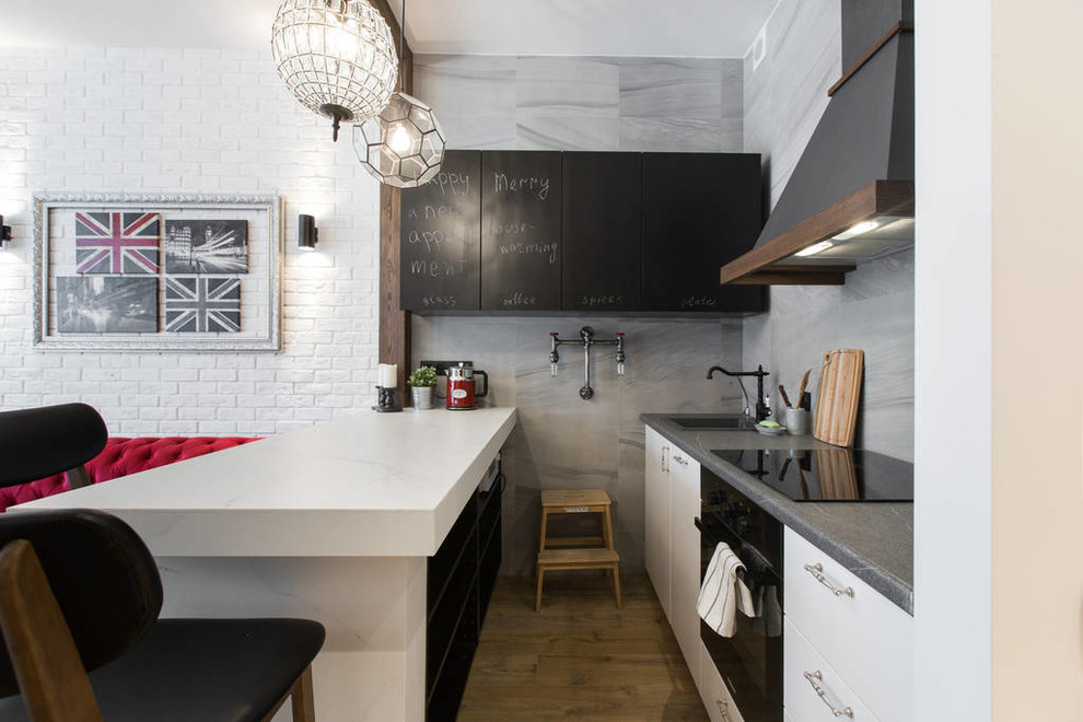 Идея дизайна: п-образная кухня-гостиная в стиле фьюжн с накладной мойкой, плоскими фасадами, серым фартуком, черной техникой, полуостровом и серой столешницей