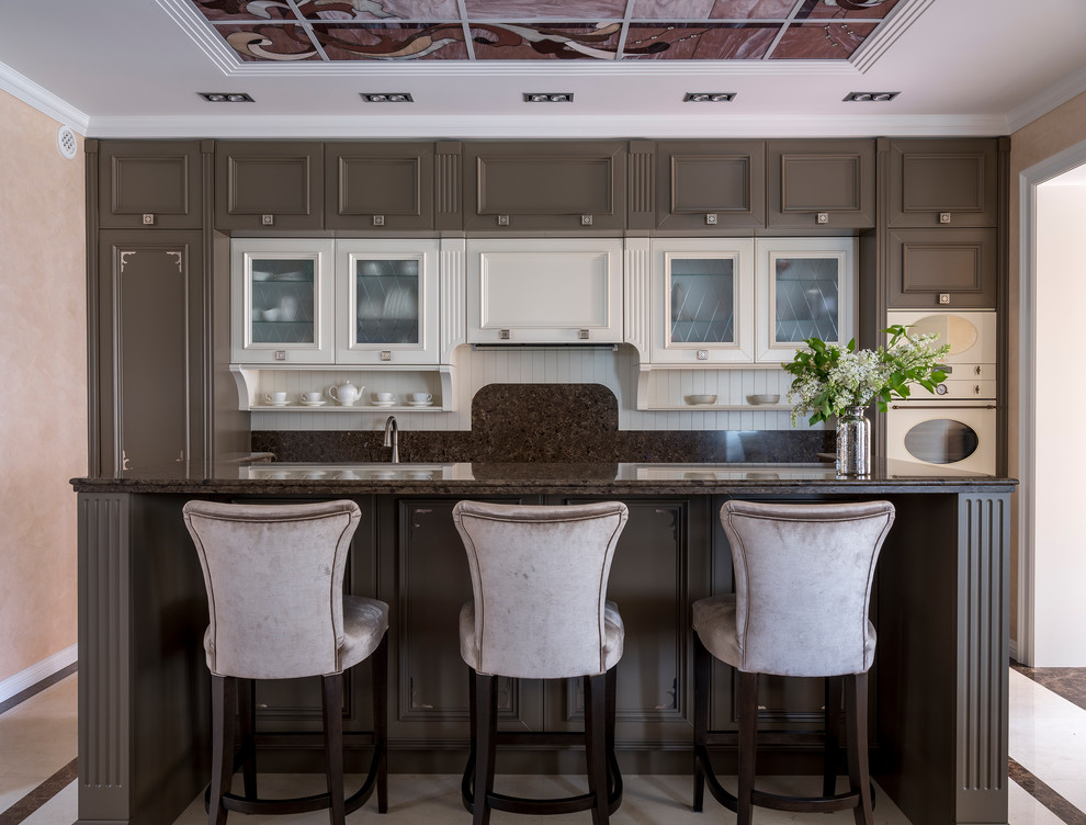Пример оригинального дизайна: прямая кухня-гостиная в стиле неоклассика (современная классика) с фасадами с утопленной филенкой, коричневыми фасадами, коричневым фартуком, белой техникой, островом и коричневой столешницей
