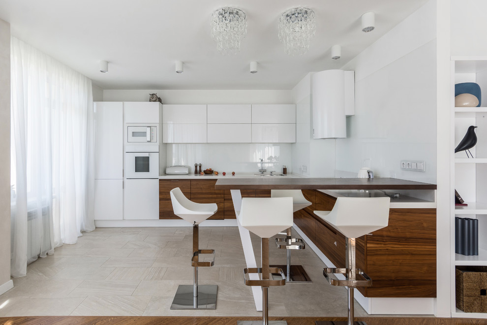 Идея дизайна: п-образная кухня-гостиная в современном стиле с плоскими фасадами, фасадами цвета дерева среднего тона, белым фартуком, белой техникой, белым полом и белой столешницей