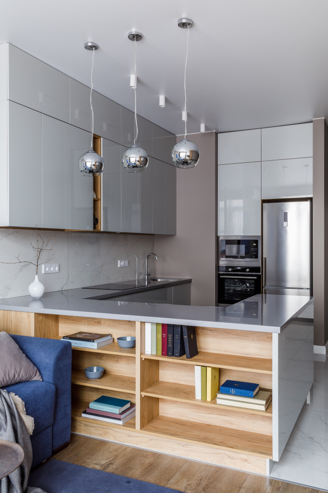 Идея дизайна: п-образная кухня-гостиная в современном стиле с врезной мойкой, плоскими фасадами, серыми фасадами, белым фартуком, техникой из нержавеющей стали, полуостровом, белым полом и серой столешницей