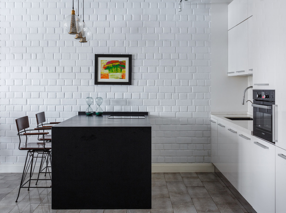 Стильный дизайн: прямая кухня-гостиная в современном стиле с врезной мойкой, плоскими фасадами, белыми фасадами, белым фартуком, черной техникой, островом и серым полом - последний тренд