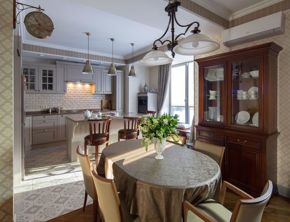 Пример оригинального дизайна: угловая кухня в классическом стиле с обеденным столом, фасадами с утопленной филенкой, серыми фасадами, бежевым фартуком, островом, серым полом и обоями на стенах