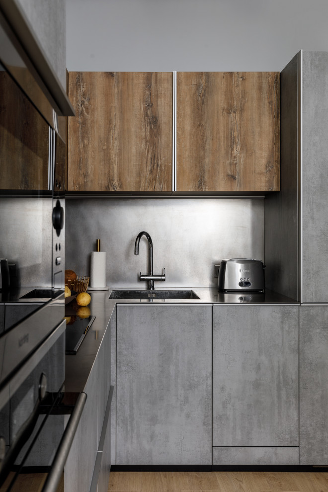 Foto de cocina contemporánea pequeña sin isla con fregadero de un seno, puertas de armario grises, encimera de acero inoxidable, salpicadero verde, electrodomésticos con paneles y encimeras grises
