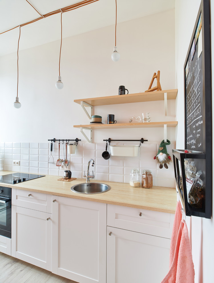 Inspiration för ett litet, avskilt minimalistiskt linjärt kök, med en nedsänkt diskho, luckor med upphöjd panel, vita skåp, vitt stänkskydd, stänkskydd i tunnelbanekakel och svarta vitvaror