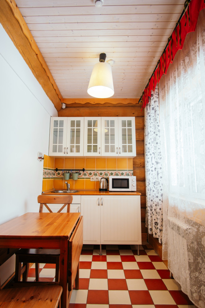 他の地域にある小さなおしゃれなキッチン (ドロップインシンク、ガラス扉のキャビネット、白いキャビネット、オレンジのキッチンパネル、セラミックタイルのキッチンパネル、セラミックタイルの床、オレンジのキッチンカウンター) の写真
