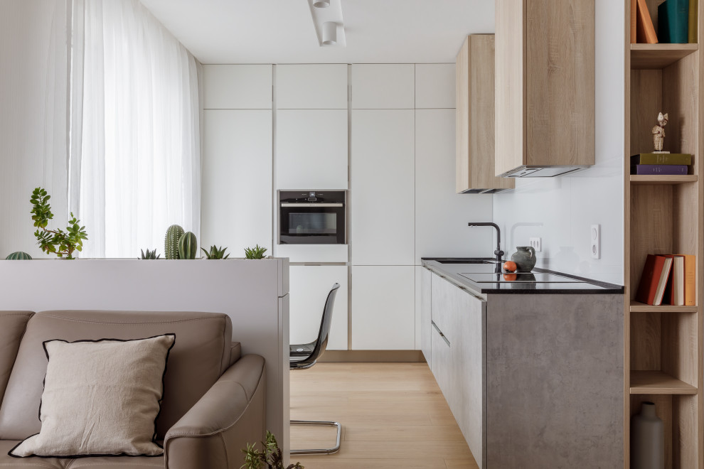 Medium sized contemporary l-shaped kitchen/diner in Other with a submerged sink, flat-panel cabinets, grey cabinets, no island, beige floors, black worktops, white splashback and black appliances.