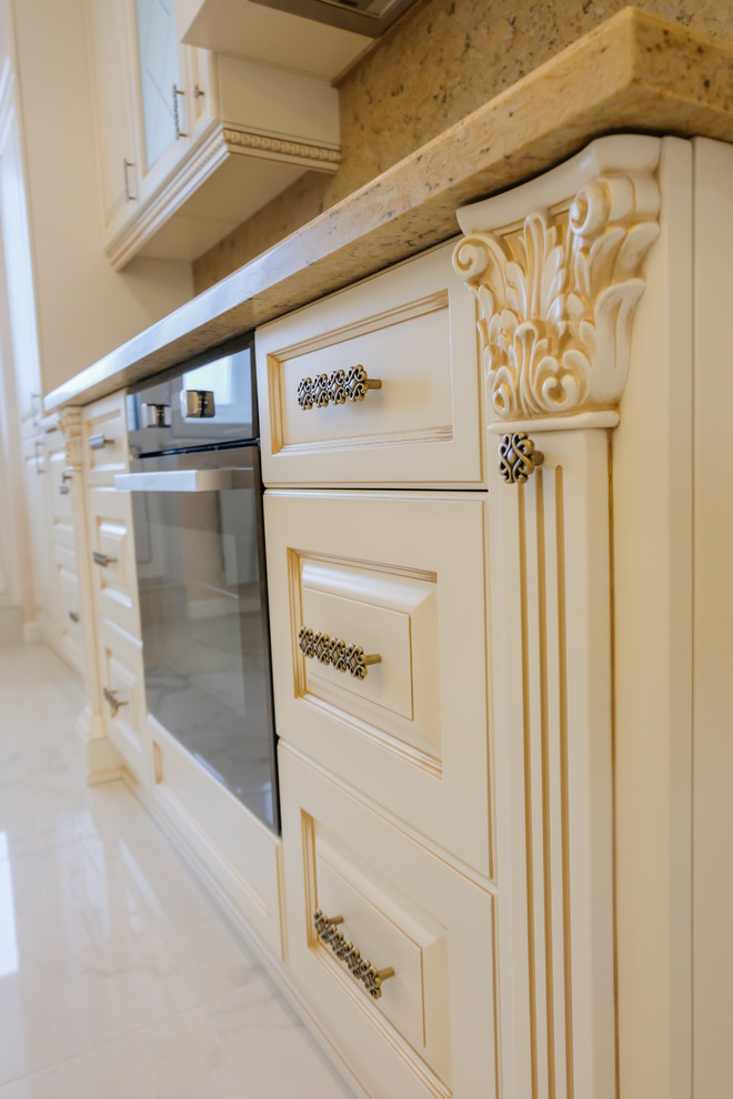 Photo of a large classic galley open plan kitchen in Moscow with raised-panel cabinets, beige cabinets, engineered stone countertops, brown splashback, marble splashback, black appliances, marble flooring, an island, beige floors and brown worktops.