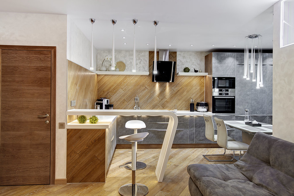 На фото: угловая кухня-гостиная в современном стиле с плоскими фасадами, серыми фасадами, коричневым фартуком, техникой из нержавеющей стали и коричневым полом