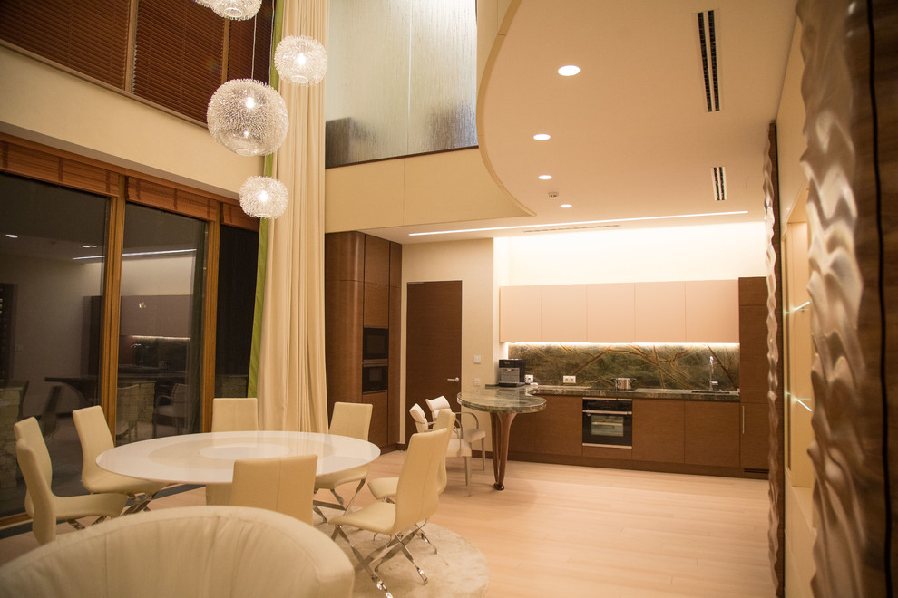 Пример оригинального дизайна: угловая кухня-гостиная среднего размера в современном стиле с монолитной мойкой, мраморной столешницей, коричневым фартуком, черной техникой, светлым паркетным полом, бежевым полом и зеленой столешницей